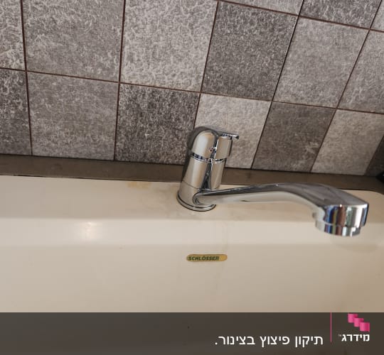 כיור עם ברז על רקע קיר אריחים אפור